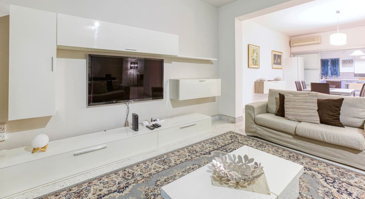 A modern living room with a flat-screen TV, white cabinetry, a beige sofa, and a patterned rug.
