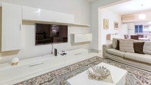 A modern living room with a flat-screen TV, white cabinetry, a beige sofa, and a patterned rug.