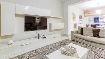 A modern living room with a flat-screen TV, white cabinetry, a beige sofa, and a patterned rug.