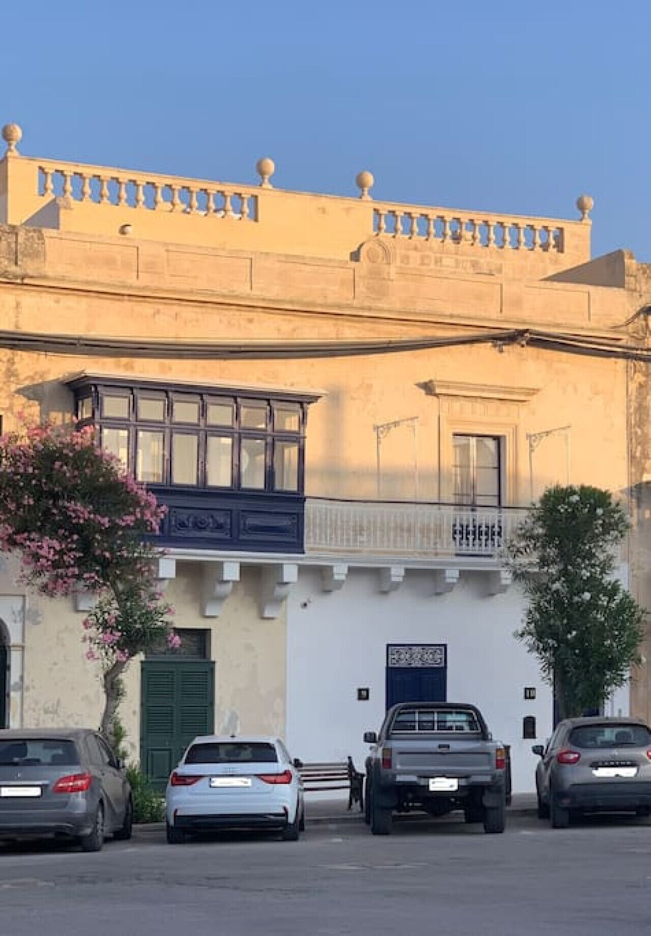 Ein Gebäude mit Balkon, einer blauen Tür und parkenden Autos davor.