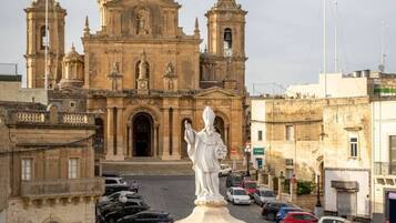 A historic building with a large dome and two bell towers, surrounded by parked cars and a statue in the foreground.