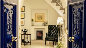 Une entrée somptueuse, agrémentée d’un lustre, d’une cheminée et d’un fauteuil en cuir noir.
