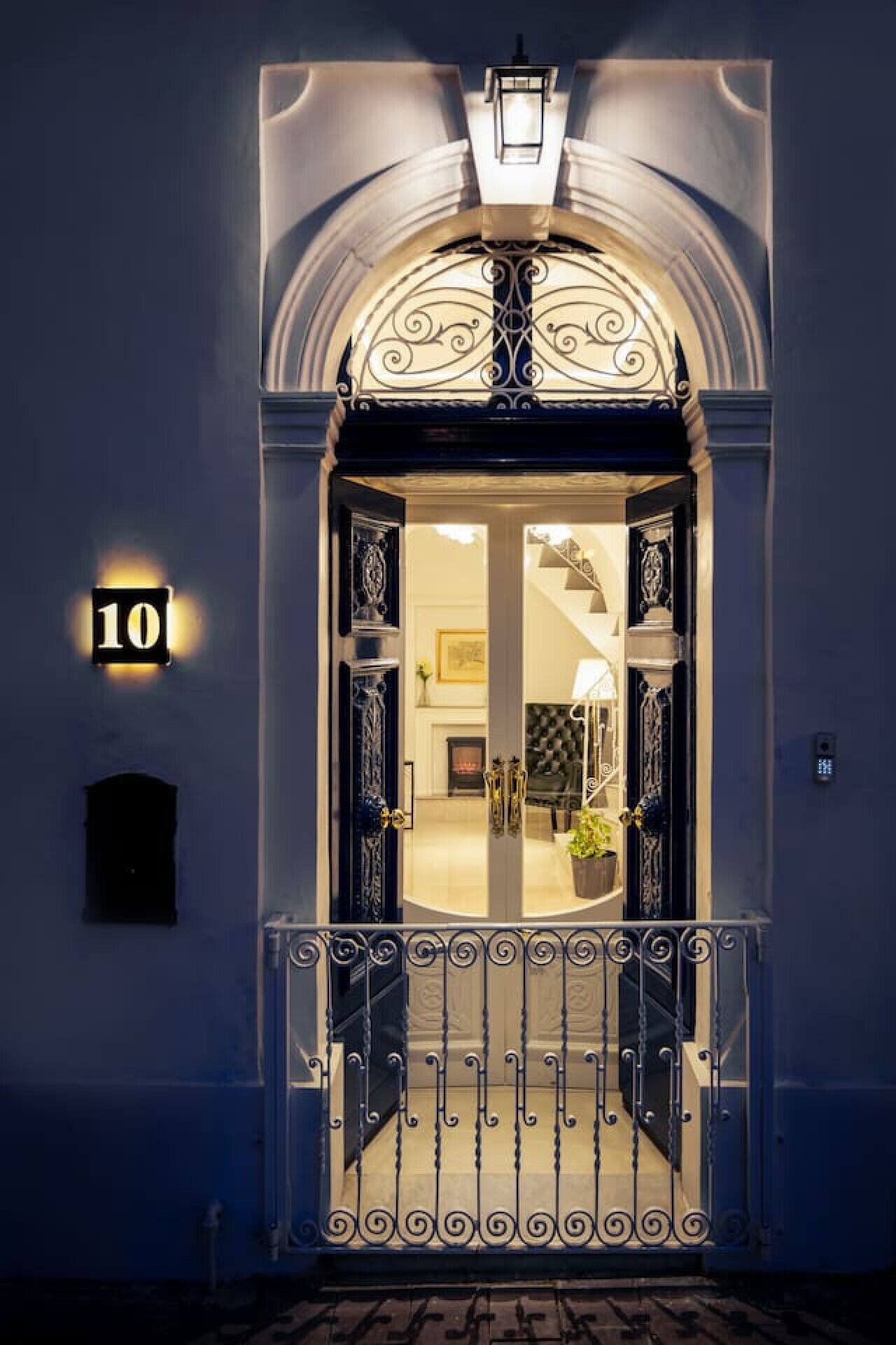 Un'imponente ingresso con un cancello in metallo decorato, un'insegna illuminata e un interno ben visibile con un camino e arredi.