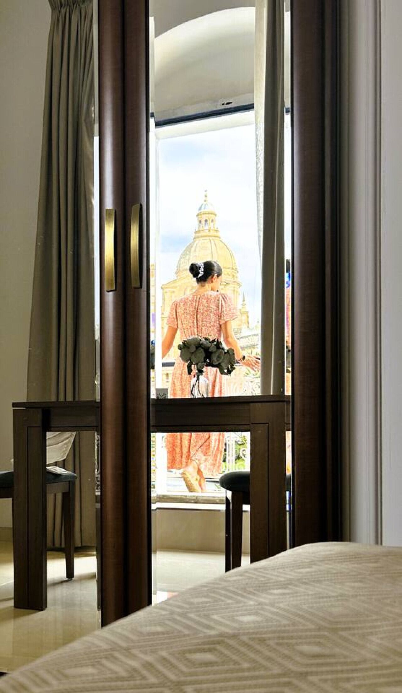 Una camera d'albergo con un letto grande, una sedia di legno e vista su un edificio con una cupola.