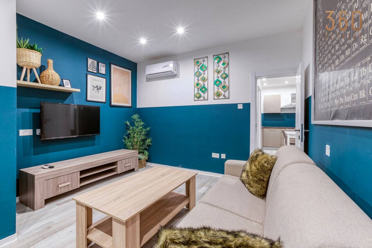 Una sala de estar moderna con una pared azul de acento, un televisor de pantalla plana, una mesa de centro de madera y un sofá beige con una manta de piel.