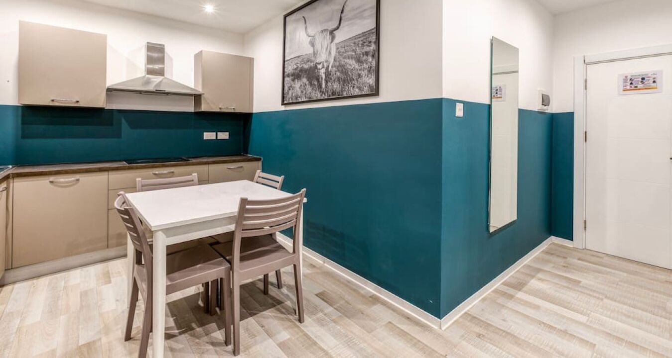 A modern kitchen with a dining table and chairs, a large mirror, and a blue accent wall.