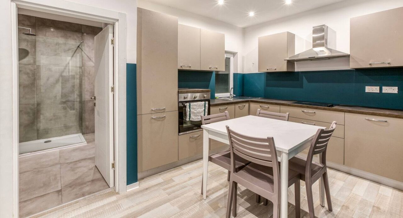 A modern kitchen with a dining area, featuring a built-in oven, a stainless steel range hood, and a large window.
