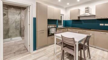A modern kitchen with a dining area, featuring a built-in oven, a stainless steel range hood, and a large window.