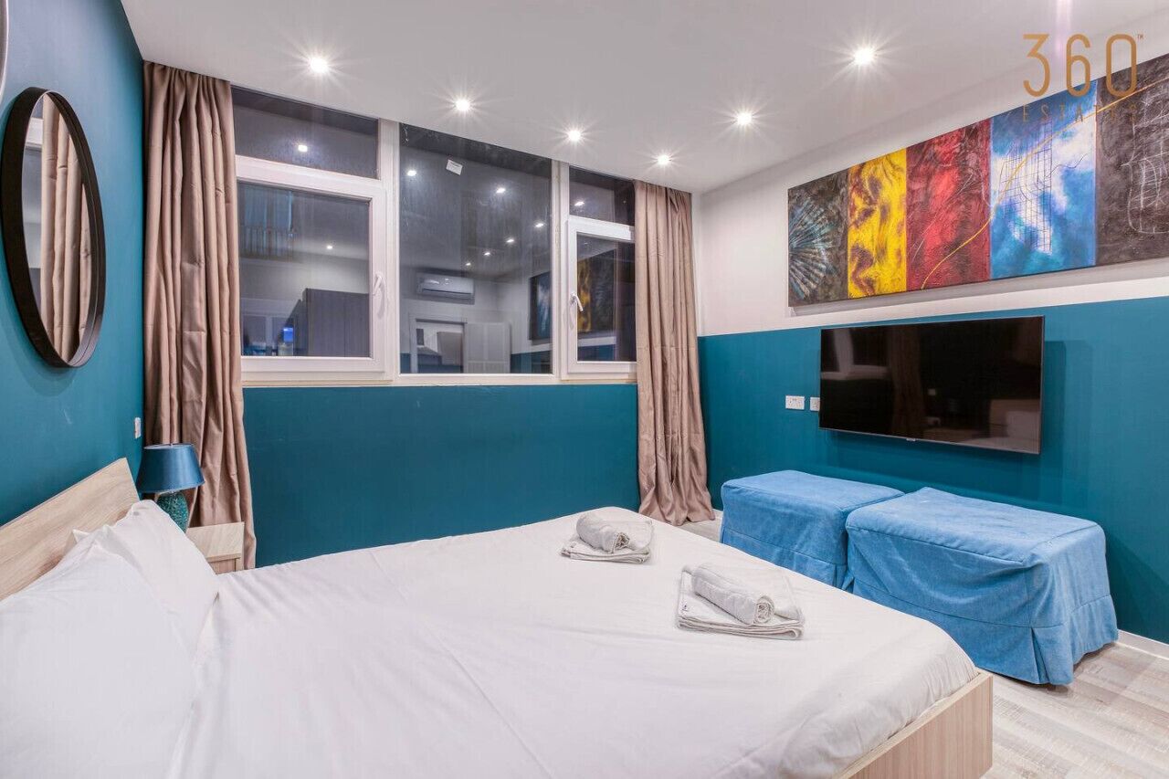 Ein Hotelzimmer mit einem Bett, zwei Nachttischen, einem Fernseher und einem großen Fenster mit Vorhängen.