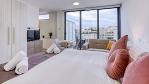 A modern hotel room with a large bed, a TV, a balcony with a view of the city, and a small desk area. - A lovely, studio penthouse with private balcony (San Ġiljan)