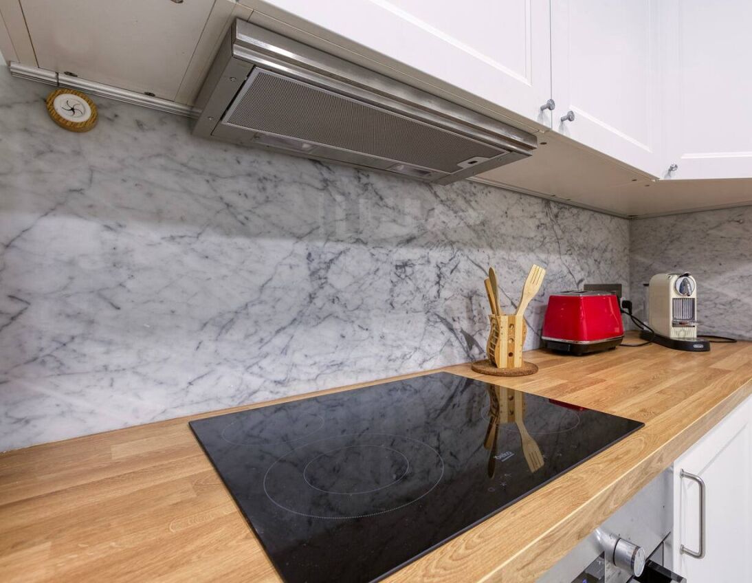 A kitchen with a black induction cooktop, white marble backsplash, and a red appliance on the counter.