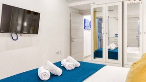 A hotel room with a bed, a TV mounted on the wall, a wardrobe, and a shower area.