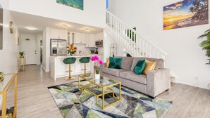 A modern living room with a grey sofa, green chairs, a glass coffee table, and a colorful rug.