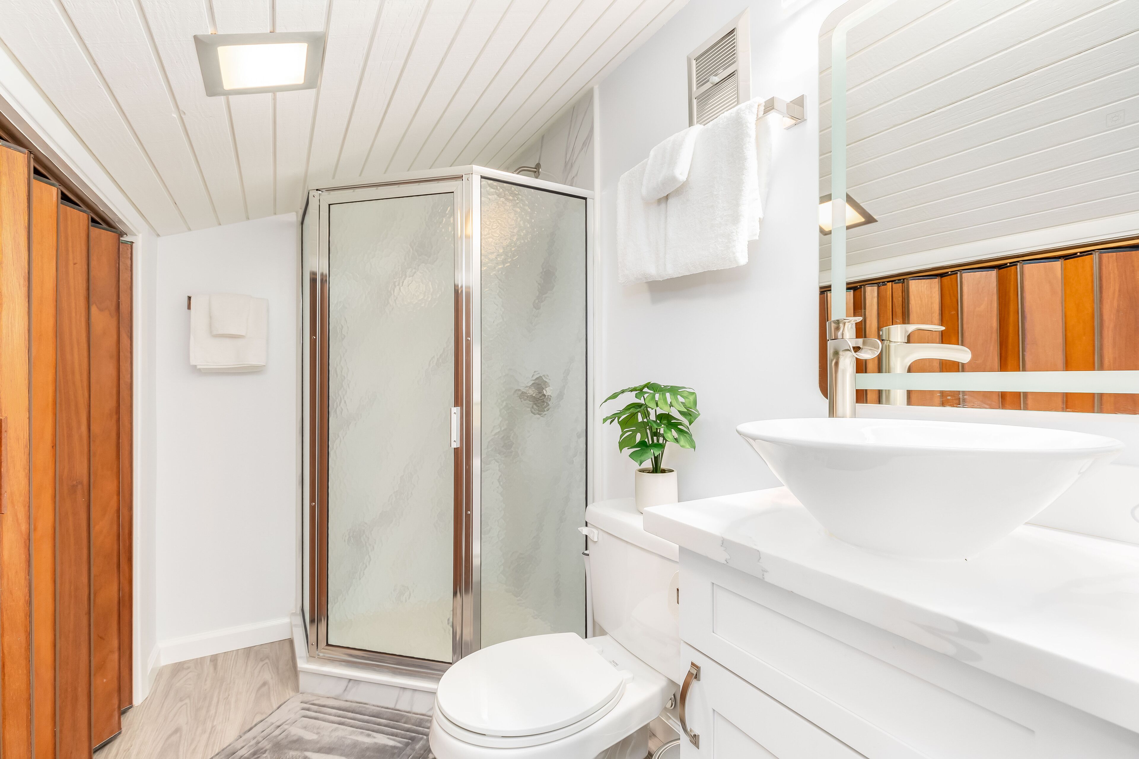 A modern bathroom with a glass shower enclosure, a white sink, and a wooden vanity.