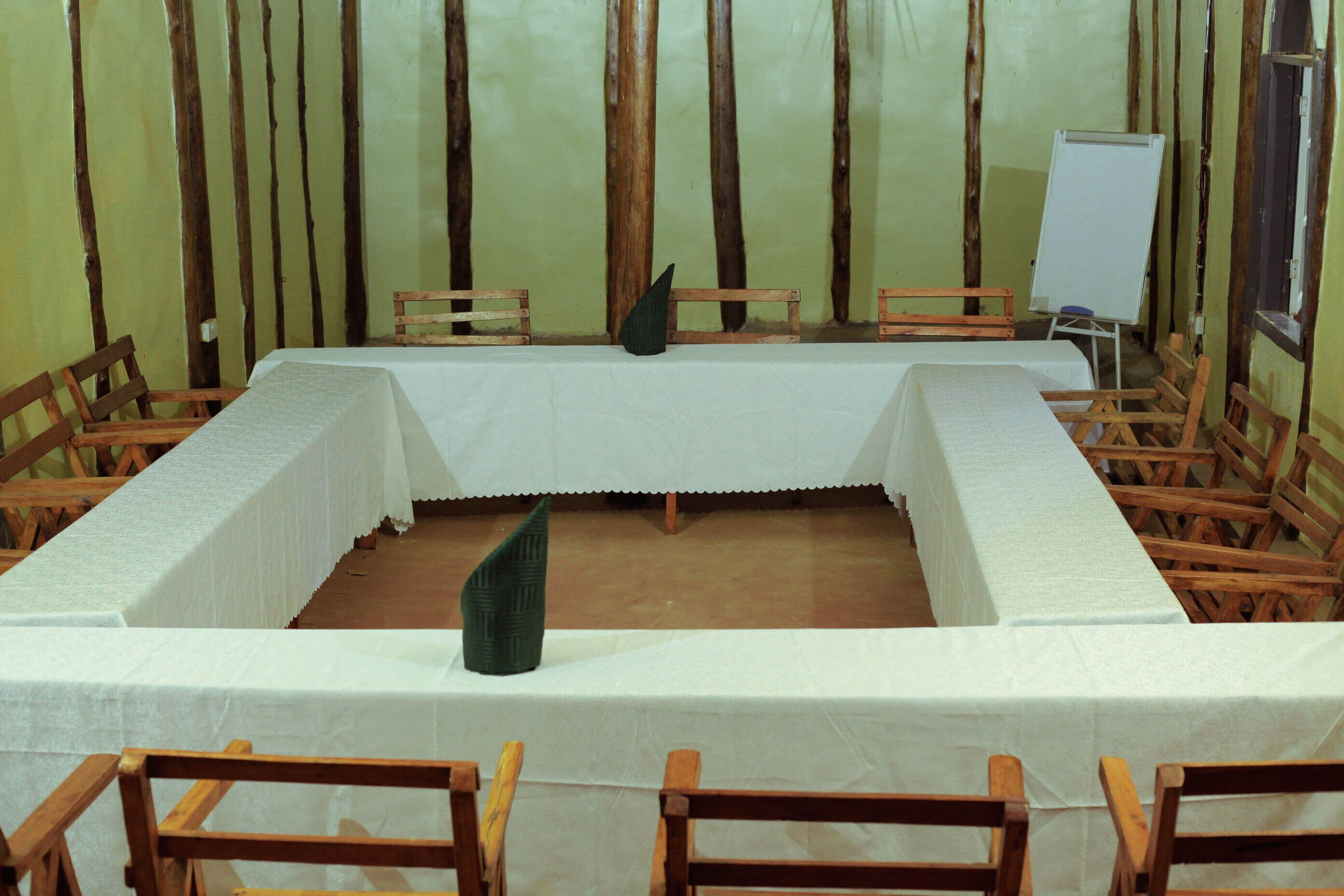 A room with a long rectangular table covered with a white tablecloth, surrounded by wooden chairs.
