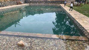 A rectangular pool with a pebble-lined edge, surrounded by a stone wall and a paved walkway. - Nyungu Yamawe Forest Park (Kitukutwe)