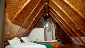 A cozy attic bedroom with a wooden sloped ceiling, a bed with white bedding, and a small window. - Nyungu Yamawe Forest Park (Kitukutwe)