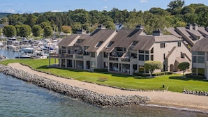 A marina with boats, a row of townhouses with balconies, and a grassy area with a picnic table.
