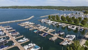 A marina with numerous boats docked, surrounded by a waterfront area with trees and a distant shoreline.