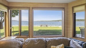 A room with large windows overlooking a lake, a wooden ceiling, and a sofa with cushions.