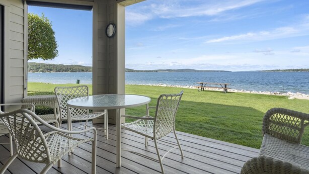 A covered outdoor patio with wicker furniture, a round table, and a view of a lake and distant shoreline.