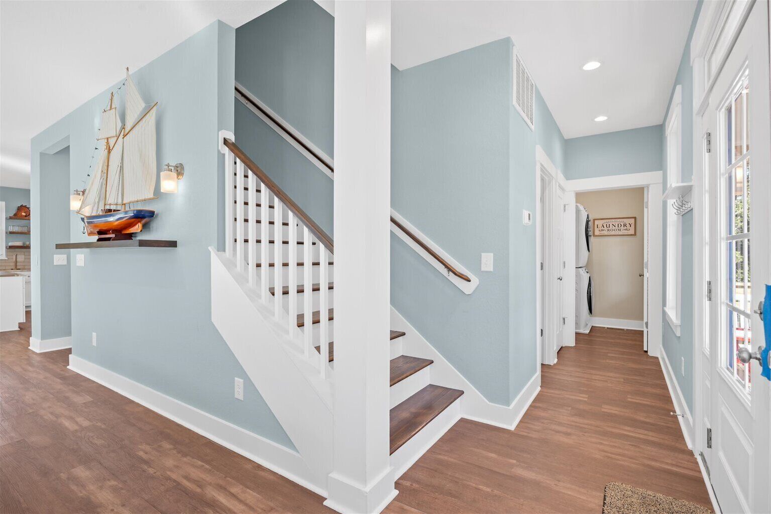Un pasillo con una escalera, un letrero que indica lavandería y un velero decorativo en la pared.