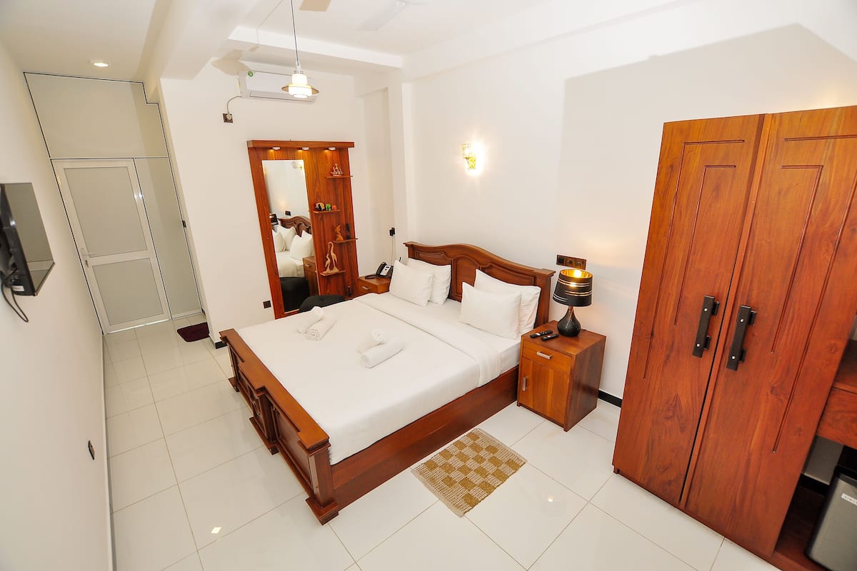 Quarto com cama grande, guarda-roupa de madeira e mesa de cabeceira com abajur.
