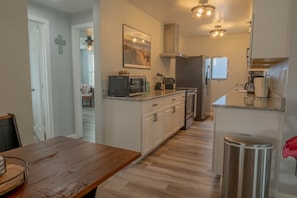 Eine kleine Küche mit weißen Schränken, einer Mikrowelle, einem Toaster und einem Kühlschrank aus Edelstahl.