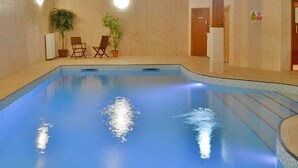 An indoor swimming pool with a tiled floor, two potted plants, and two wooden chairs.