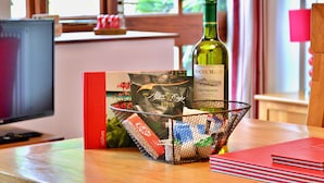 A table with a bottle of wine, a gift basket, and a red book. - Little Dunley - Wisteria Cottage (Bovey Tracey)