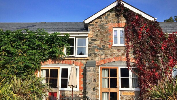 A stone cottage with two windows, a door, and a small patio with outdoor furniture. - Little Dunley - Wisteria Cottage (Bovey Tracey)