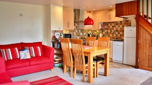 A compact living space with a red sofa, wooden dining table, and chairs, a kitchen with a microwave, dishwasher, and a red pendant light. - Little Dunley - Wisteria Cottage (Bovey Tracey)