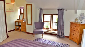 A bedroom with a bed, a desk, a chair, a dresser, a window with curtains, and a fan. - Little Dunley - Wisteria Cottage (Bovey Tracey)