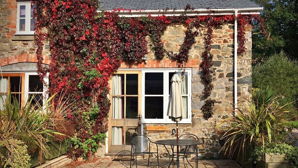 A stone cottage with ivy-covered walls, a small patio with a table and chairs, and a sign reading "Virginia Cottage." - Little Dunley - Virginia Cottage (Bovey Tracey)