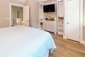 Une chambre à coucher comprenant un lit, un téléviseur fixé au mur, une commode et une armoire.