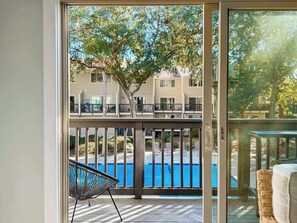 A balcony with a view of a swimming pool and a tree.