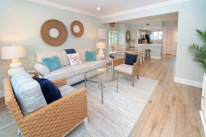 A living room with a sofa, wicker chairs, a glass coffee table, and a dining area with a bar.