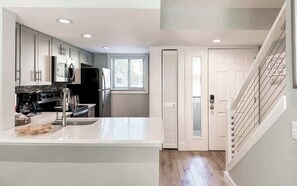 A modern kitchen with stainless steel appliances, a white countertop, and a wooden cutting board.