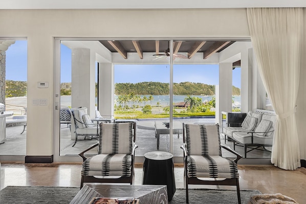 A spacious balcony with a view of a beach and hills, furnished with two chairs and a table.