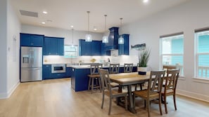 A modern kitchen with blue cabinets, stainless steel appliances, pendant lighting, and a dining area with wooden chairs and a table. - Beachview Oasis: 5  BR, 3.5  BA House in Crystal Beach, Sleeps 16 (Bolivar Peninsula)