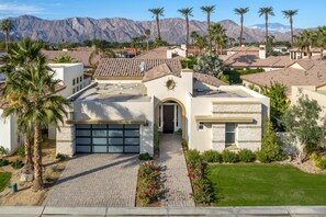 A modern house with a garage, surrounded by palm trees and mountains in the background.