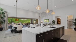 Une cuisine moderne dotée d’un grand îlot central, de meubles de rangement aux couleurs sombres et d’un éclairage suspendu.