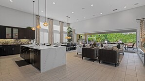 Une cuisine moderne dotée d’un grand îlot central, de meubles de couleur sombre et d’un éclairage suspendu.