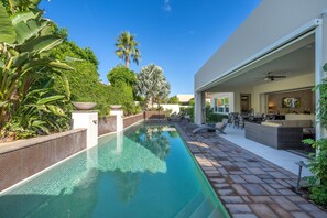 A modern outdoor pool area with a clear pool, surrounded by lush greenery and a patio with outdoor furniture.