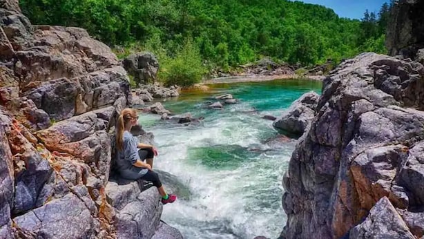 A person sitting on rocks by a flowing river surrounded by greenery. - Your home away from home in downtown, historic Farmington! (Farmington)