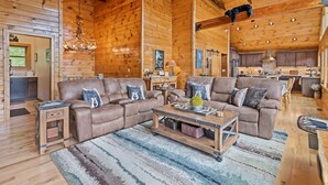 A spacious log cabin interior with a large living area featuring two sofas, a coffee table, and a chandelier. - Black Bear Ridge! Newly Built! 4BD/3.5 BA (Maggie Valley)