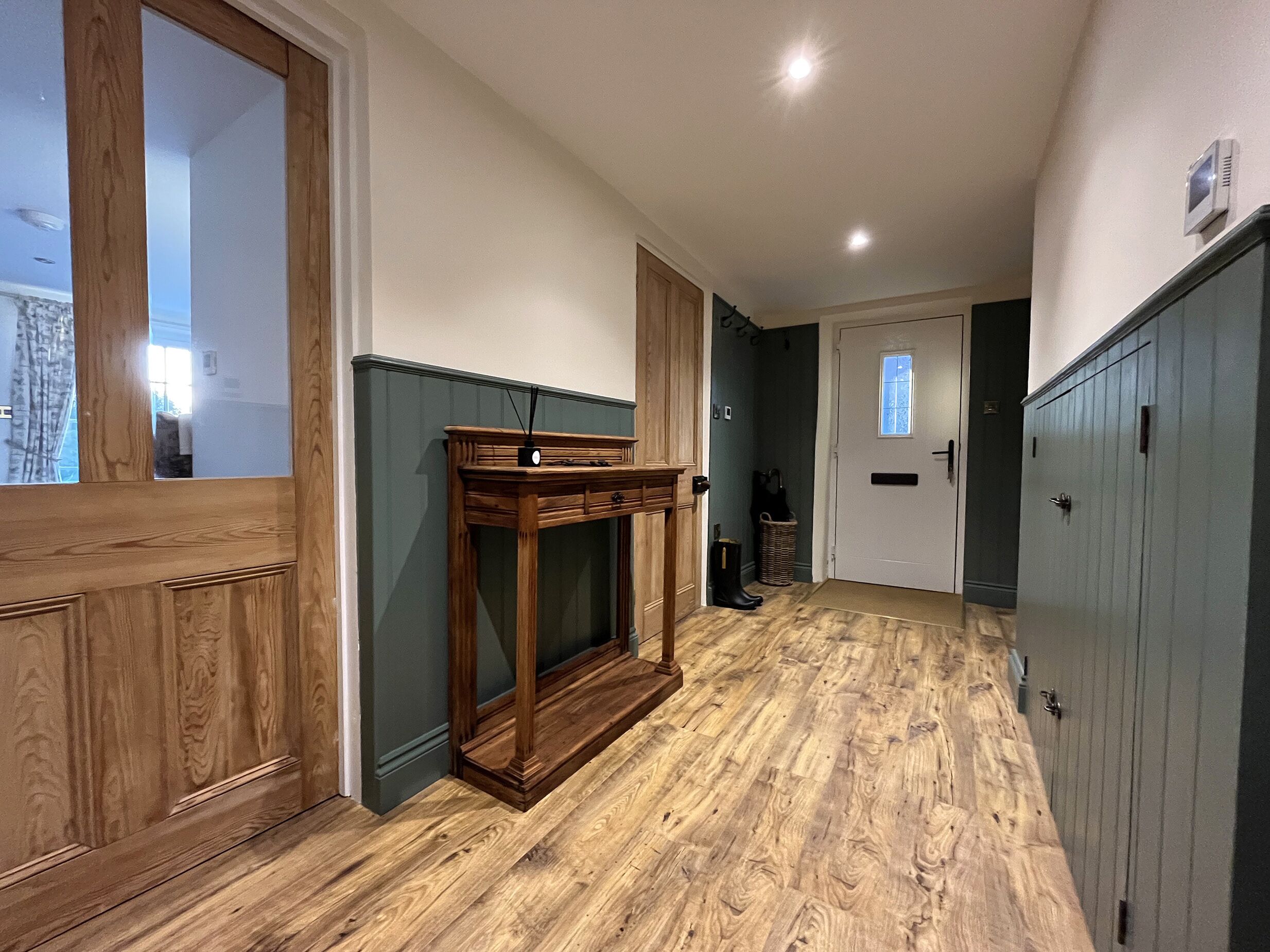 Un pasillo con piso de madera, una consola de madera y una puerta con ventanal.
