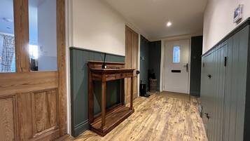 Un pasillo con piso de madera, una consola de madera y una puerta con ventanal.