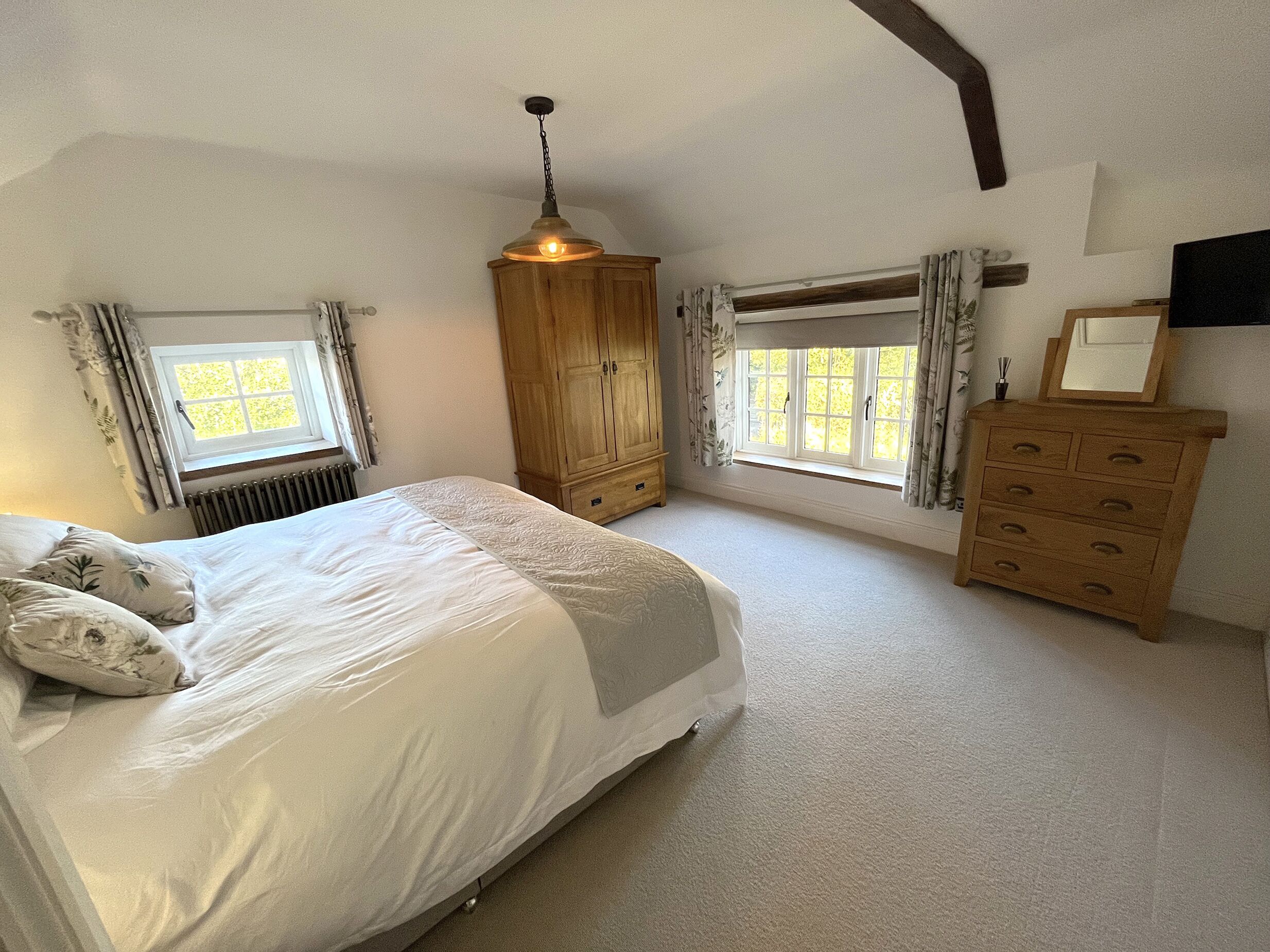 A bedroom with a large bed, wooden wardrobe, and a window with curtains.