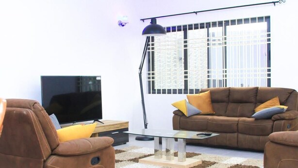 Un salon avec un canapé marron, une table basse en verre, un téléviseur et un lampadaire.